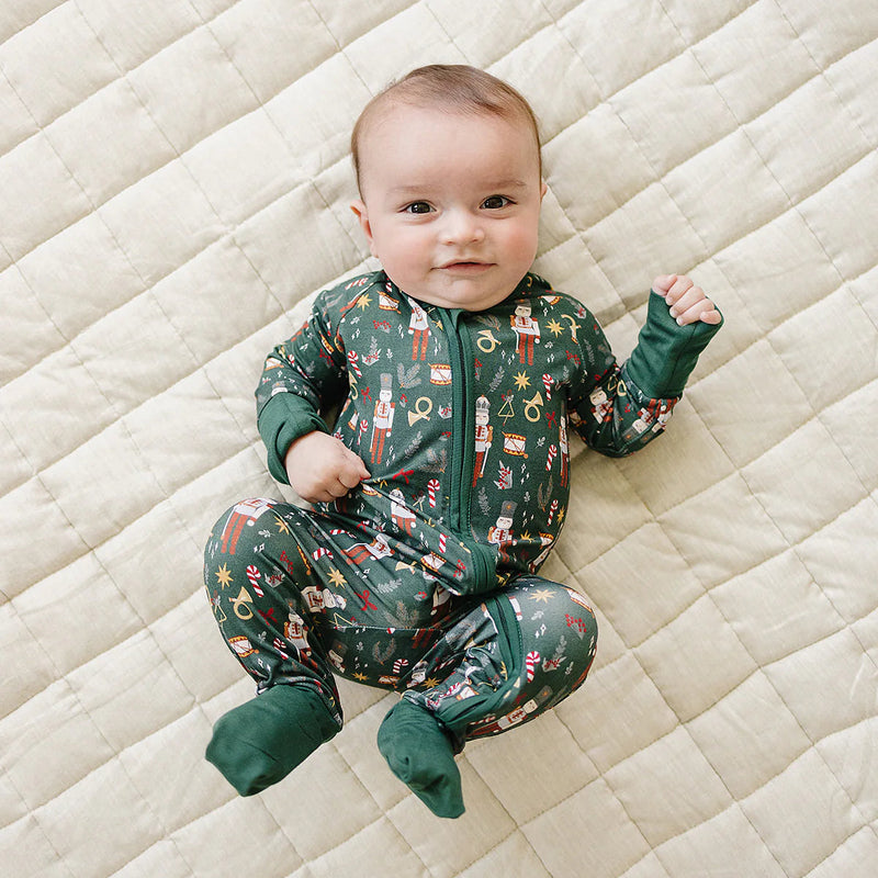 baby wearing green nutcracker bamboo coverall lying on quilted blanket