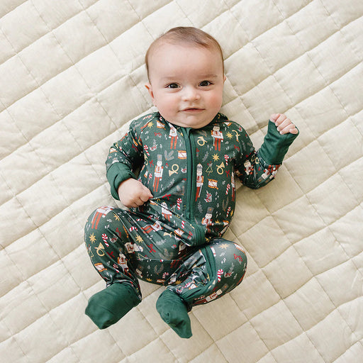 baby wearing green nutcracker bamboo coverall lying on quilted blanket