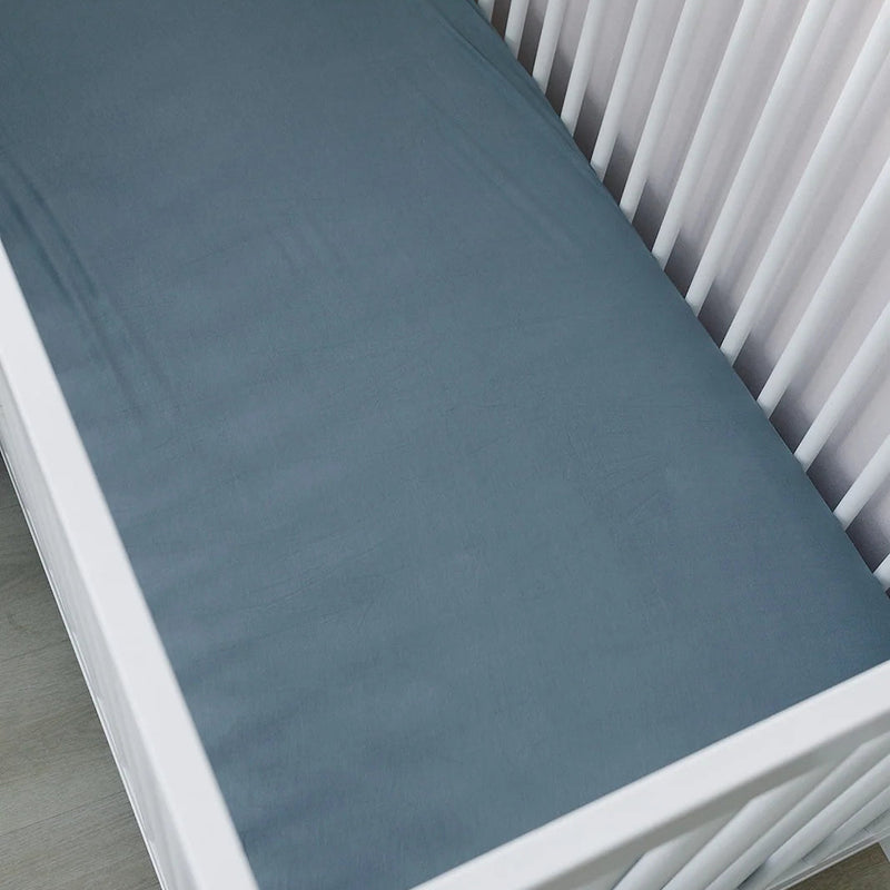 Mebie Baby Bamboo Crib Sheet in Dusty Blue on a mattress in a white crib