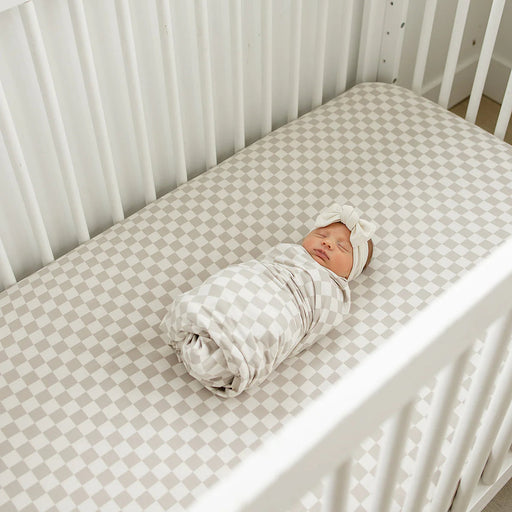 taupe checkered bamboo crib sheet styled in white crib with swaddled baby