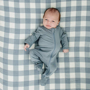 Newborn baby in a blue sleeper lying on the Mebie Baby Dusty Blue Gingham Muslin Crib Sheet