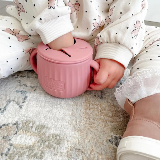 Child holding a pink cup with a brand logo on a textured surface