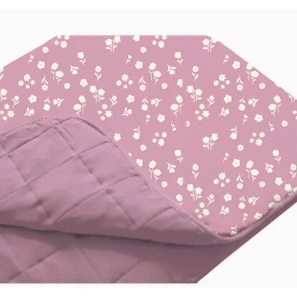 A close-up of the Mini Floral quilted blanket laid flat. One corner is folded back to show the reversible design: a soft mauve solid on one side and a dainty white floral print on a mauve background on the other.