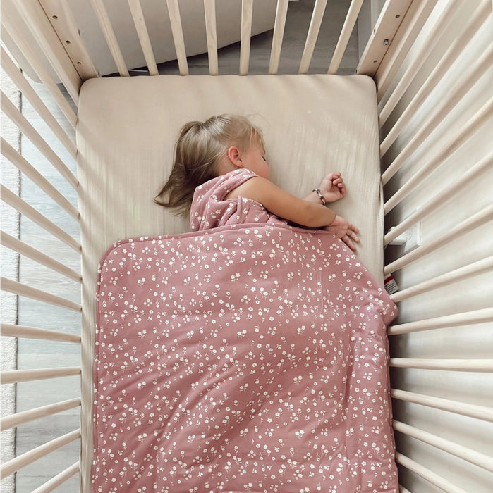 A toddler sleeps peacefully in a crib, snuggled under the Mini Floral blanket. The blanket covers the child from chest to toes and appears plush, warm, and gently textured.