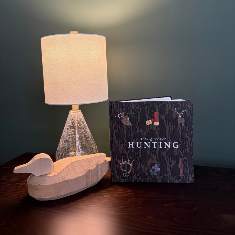 Lamp and book titled 'The Big Book of Hunting' on a table with a dark background