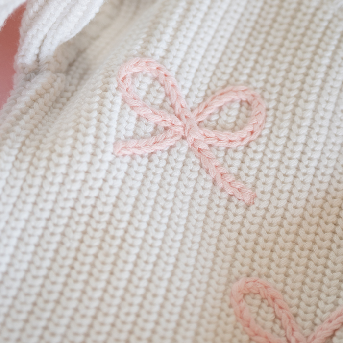 Close-up of a beige knitted fabric with pink embroidered bow design.