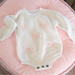 White knitted baby romper with pink bows on a pink cushion