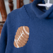 Blue sweater with a brown football patch on a hanger
