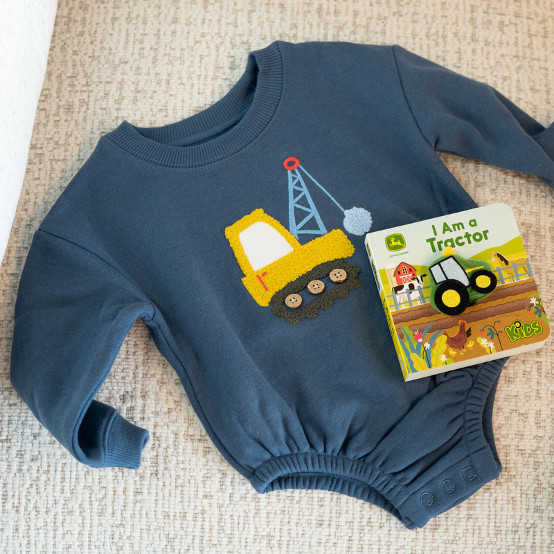 Blue baby romper with construction vehicle design and matching book on a textured surface
