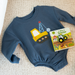 Blue baby romper with construction vehicle design and matching book on a textured surface