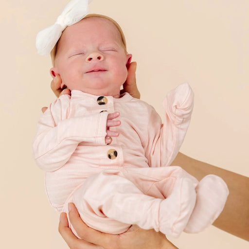 Newborn baby in a pink outfit with a white bow on a beige background