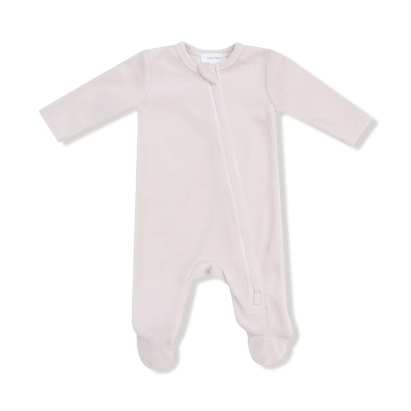 A soft oatmilk-colored velour footie with a diagonal zipper and built-in feet.