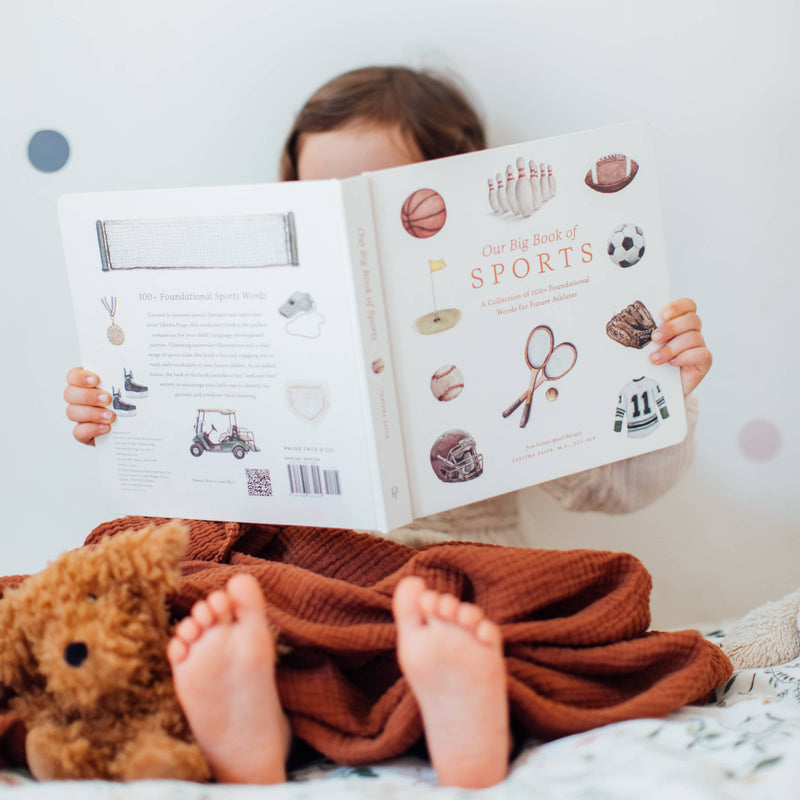 Child reading a book with a teddy bear on a bed