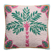A square throw pillow featuring a hand-tufted palm tree design on a pale pink background, with green leaves, a pink trunk, and a border of pink monstera leaves and light blue trim.
