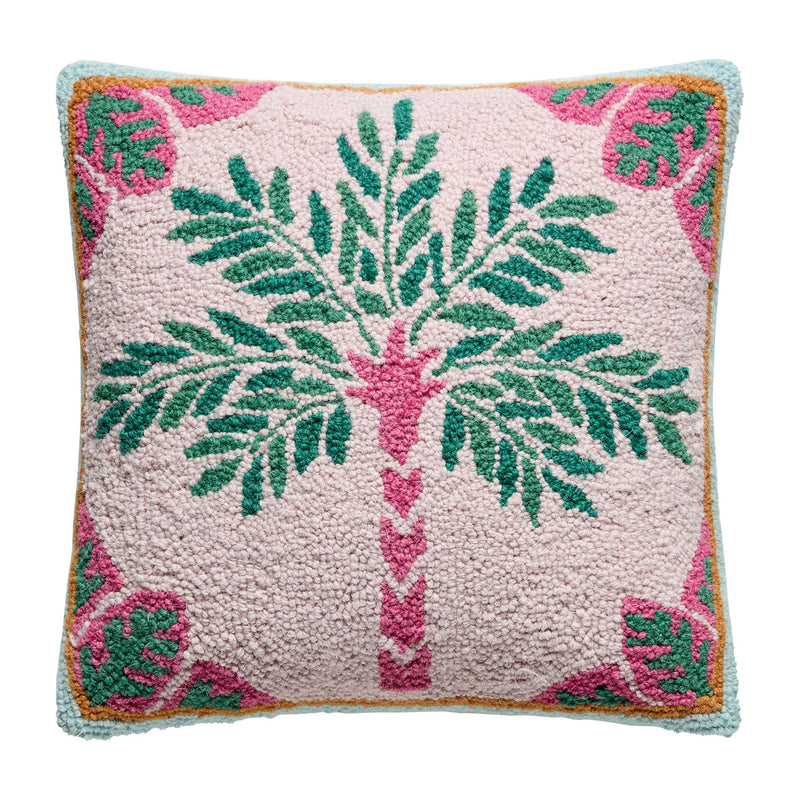 A square throw pillow featuring a hand-tufted palm tree design on a pale pink background, with green leaves, a pink trunk, and a border of pink monstera leaves and light blue trim.