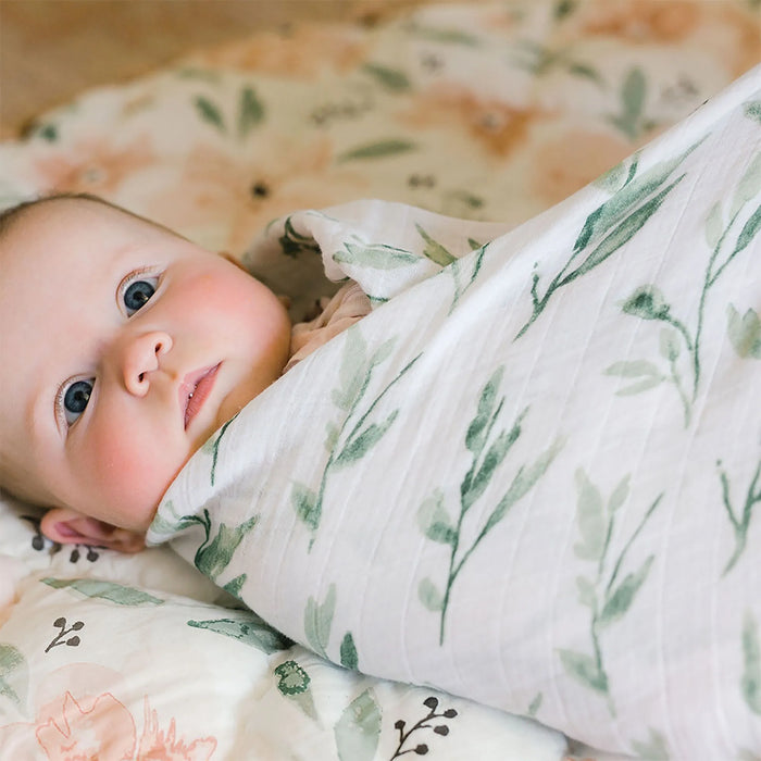 Baby swaddled in Parker floral muslin wrap lying on matching blanket