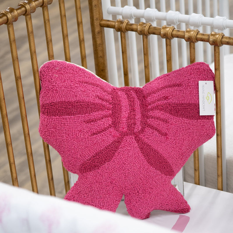 A bright pink textured bow-shaped pillow resting inside a gold and white crib.