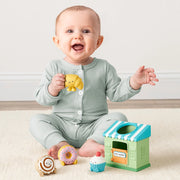 Baby sitting on the floor playing with the Itzy Play Bakery activity toy and soft bakery pieces