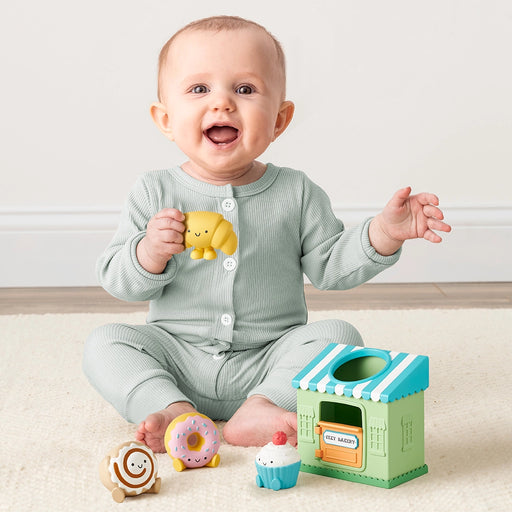 Baby sitting on the floor playing with the Itzy Play Bakery activity toy and soft bakery pieces