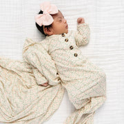 Newborn baby wrapped in a beige knitted blanket with a pink bow on a white background