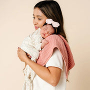 Woman holding a baby wrapped in a pink blanket against a beige background