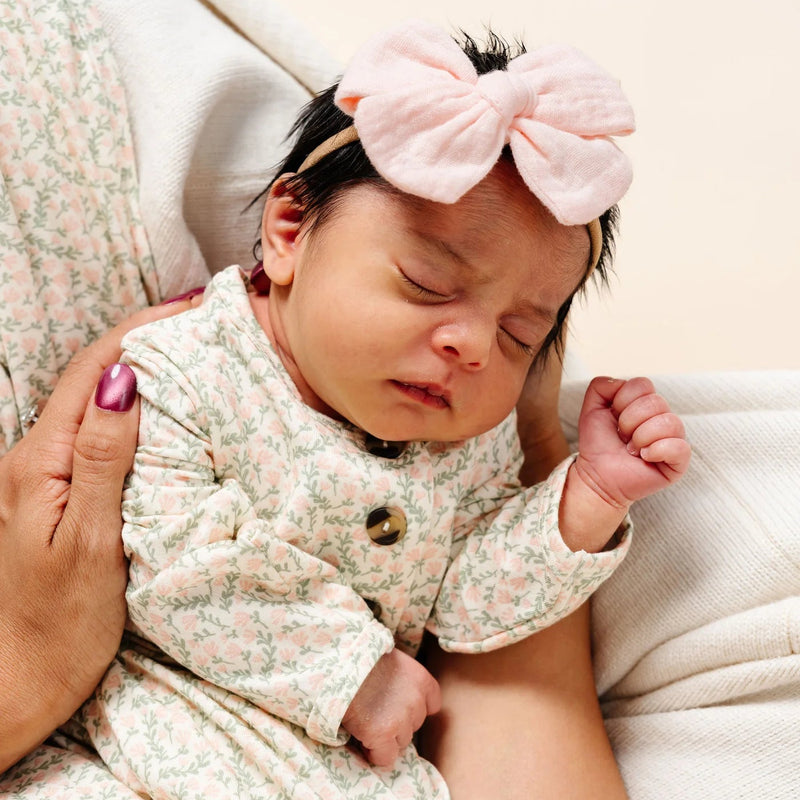 Newborn baby wearing a floral outfit and pink headband, lying on a white surface.