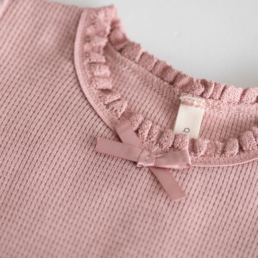 Pink textured fabric with lace trim and a bow on a light gray background