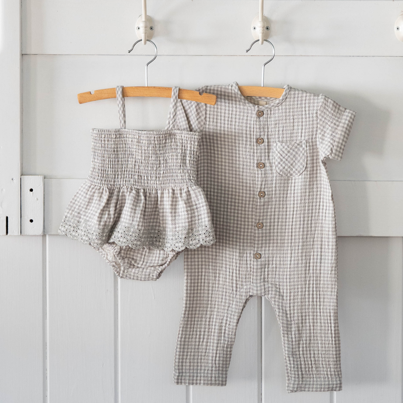 Baby romper and bloomers with buttons on hangers against a white wall.