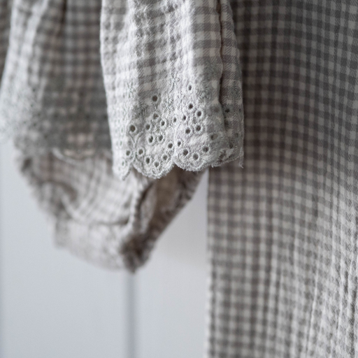 Close-up of a checkered garment with lace eyelet  trim on a white background