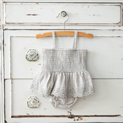 Baby romper with straps hanging on a wooden hanger against a rustic white wooden background.