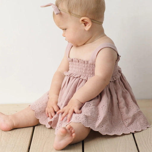 Baby in a pink dress sitting on a wooden floor with a white background