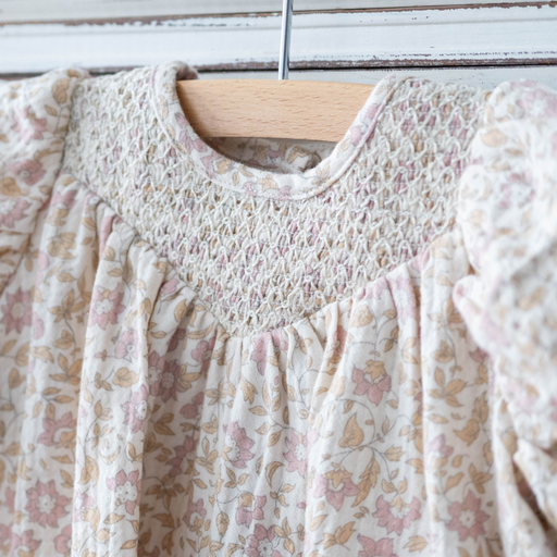 Floral patterned dress on a wooden hanger against a white wall.