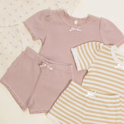 Children's clothing set with pink top, shorts, and yellow striped shirt on a light background