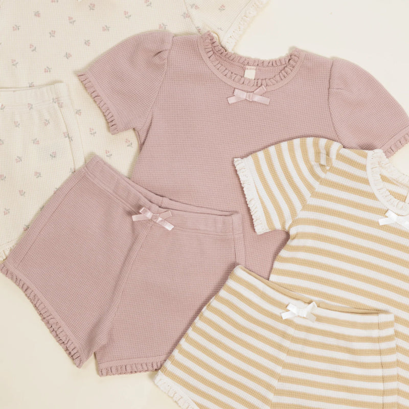 Children's clothing set with pink top, shorts, and yellow striped shirt on a light background