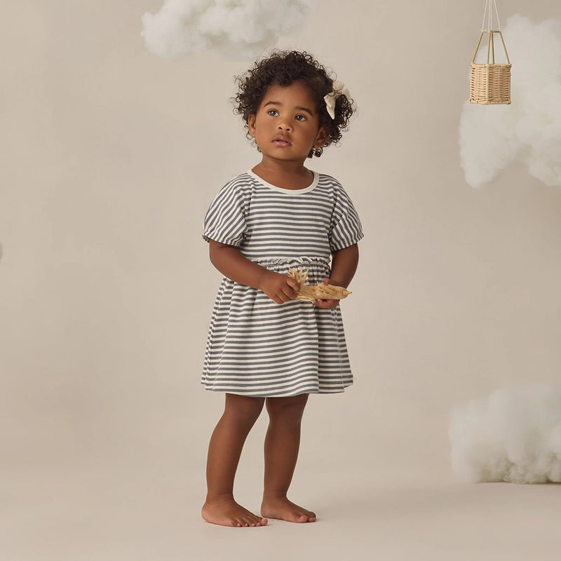 Young child wearing a striped dress holding a basket against a neutral background