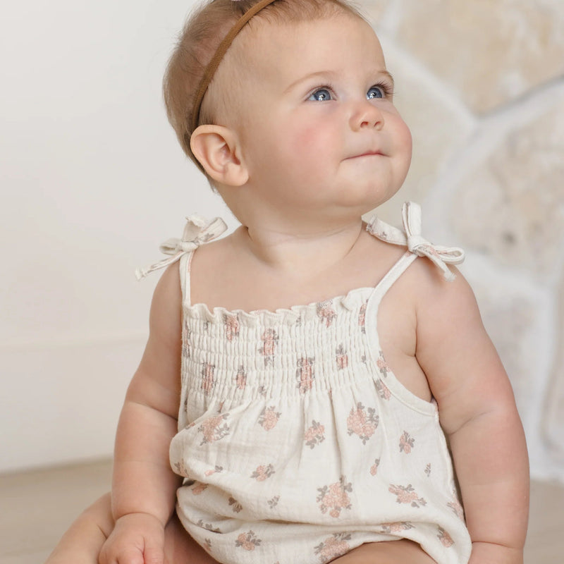 Baby wearing a floral romper with a bow headband against a neutral background