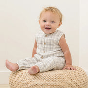 Baby sitting on a woven ottoman with a plain background