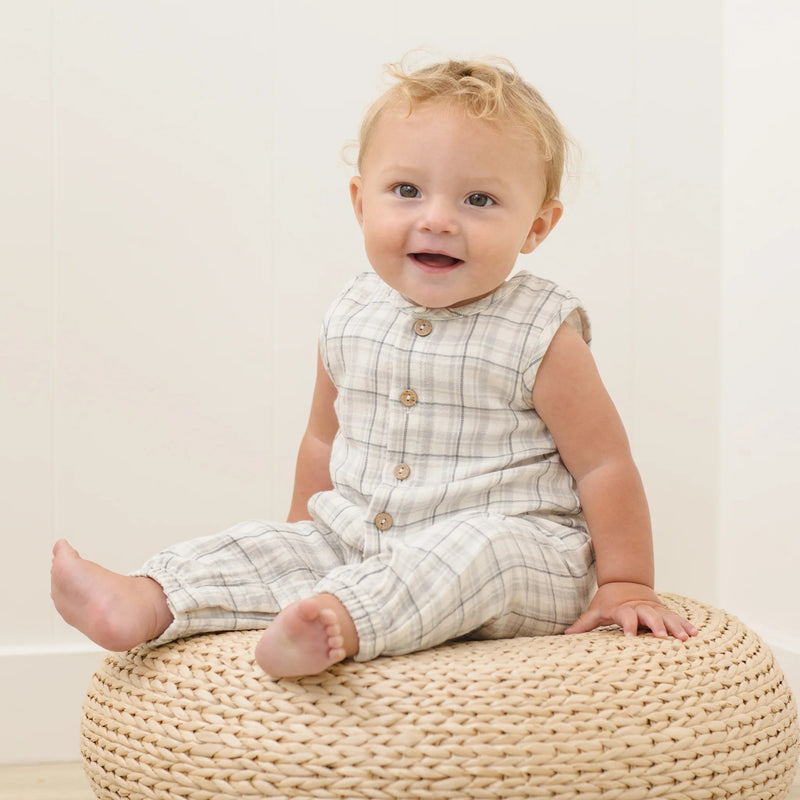 Baby sitting on a woven ottoman with a plain background
