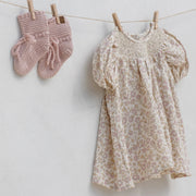 Floral dress and pink knitted mittens hanging on a clothesline against a white background