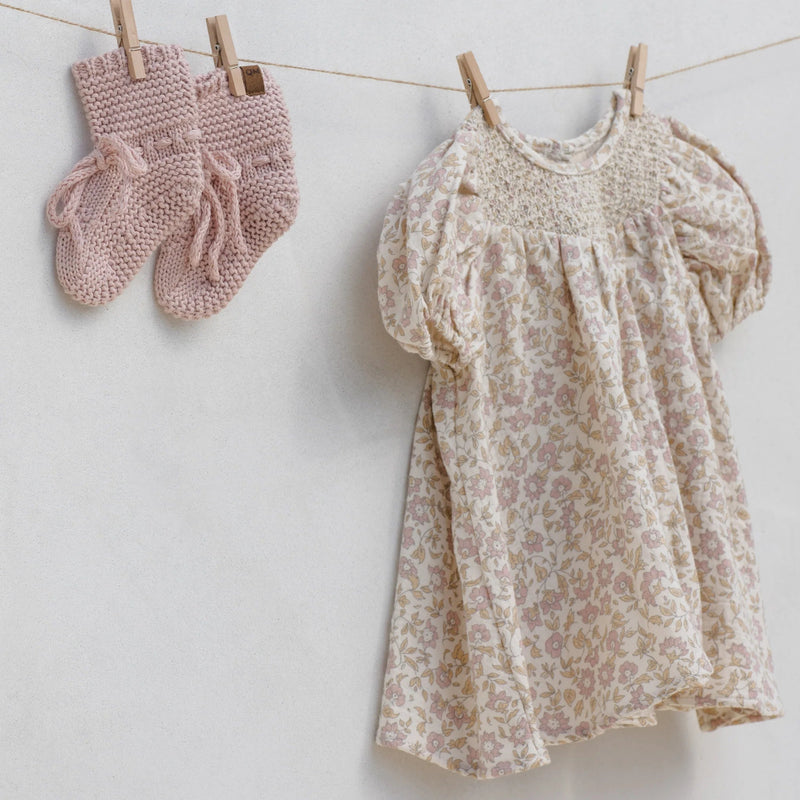 Floral dress and pink knitted mittens hanging on a clothesline against a white background