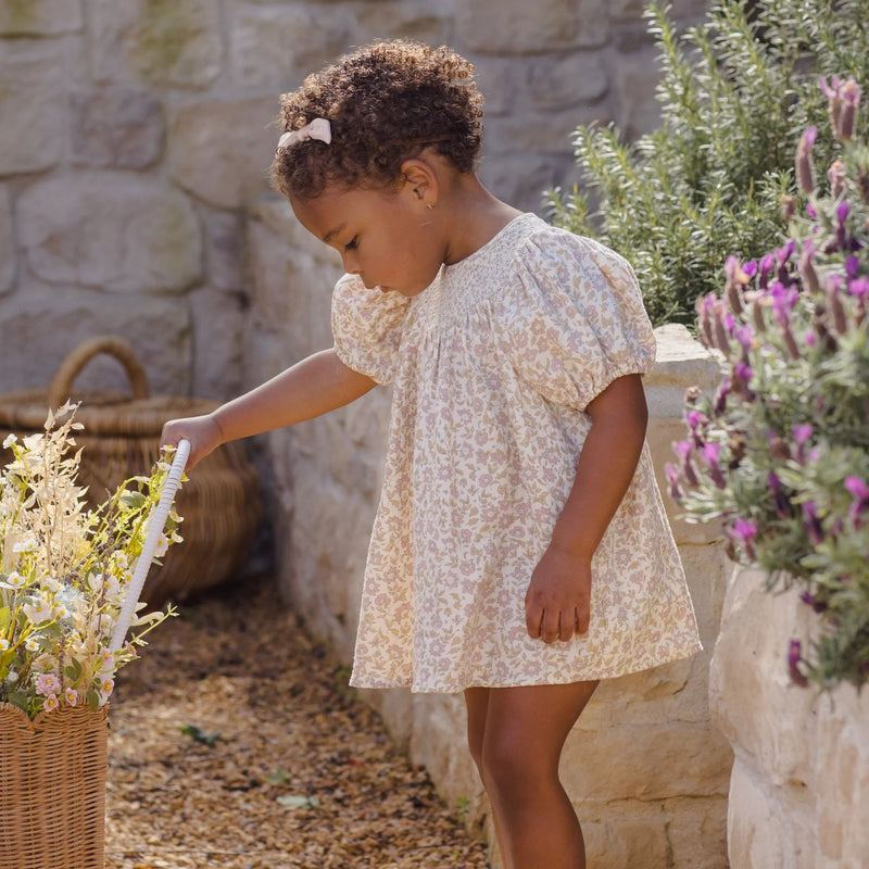 Child in a floral dress interacting with a rabbit in an outdoor setting