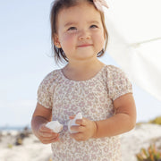 Child in a floral dress holding shells on a beach