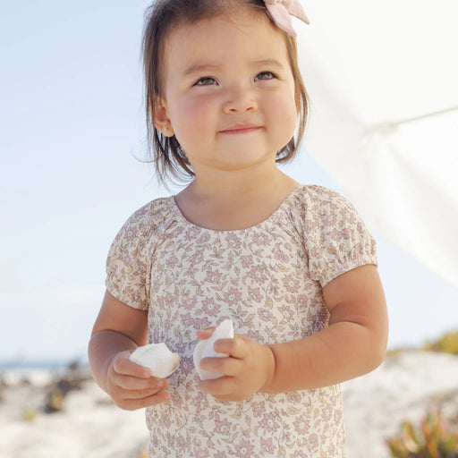 Child in a floral dress holding shells on a beach