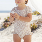 Young child in a floral bathing suit standing on a sandy beach.