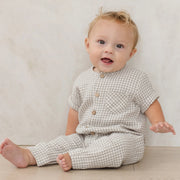 Baby wearing a checkered outfit sitting on a light-colored floor.