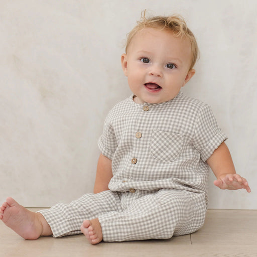 Baby wearing a checkered outfit sitting on a light-colored floor.