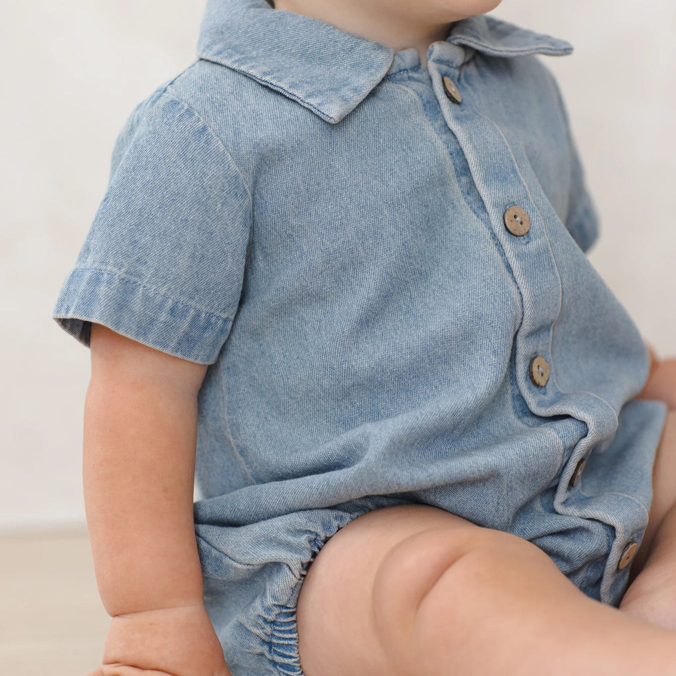 Baby wearing a denim romper with a plain background