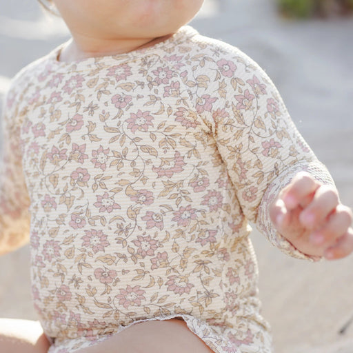Baby wearing a floral outfit with a blurred natural background