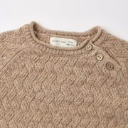 Close-up of a beige cable-knit baby sweater with a mock neck, three-quarter button closure, and a visible Quincy Mae brand label.