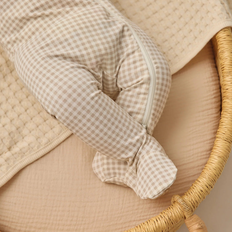 Baby outfit with checkered sleeves and quilted jacket on a wicker chair